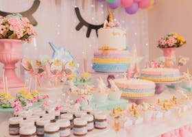 A vibrant unicorn-themed birthday party setup with cakes, cupcakes, and decorations.