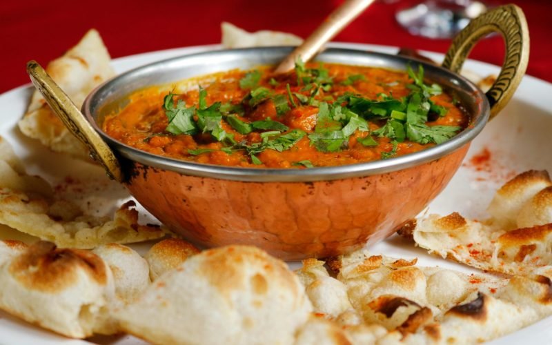 Delicious Indian curry garnished with cilantro served with naan in a copper dish.